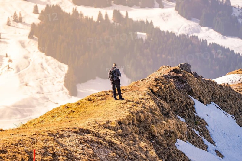A hiker stands on a snow-covered ridge and looks into the distance under a bright sun, Hochgrat Mountains, Allgäu Alps, Oberreute, Germany