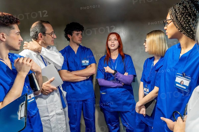 Medical professionals including doctors and nurses, wearing blue scrubs and a lab coat, standing and actively engaged in a serious discussion about healthcare in a professional setting