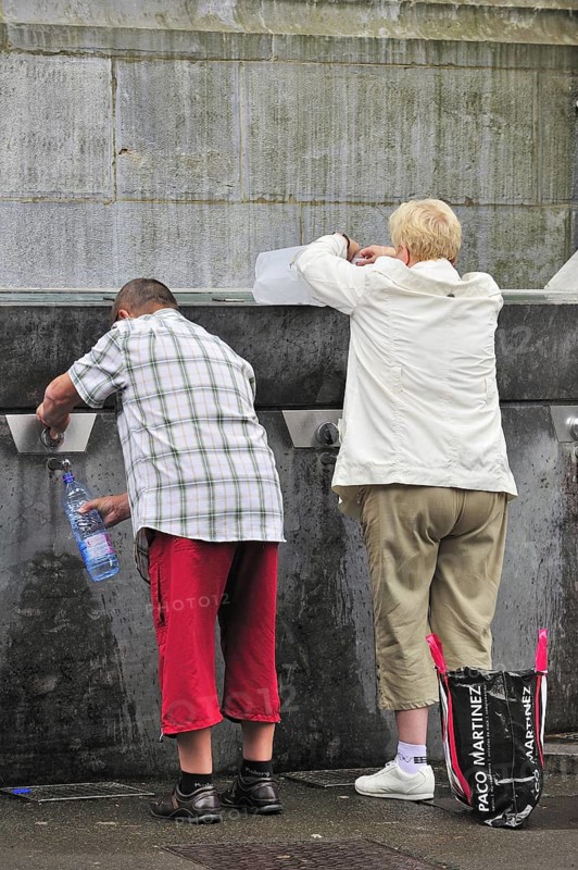 Pilgrims filling bottles with healing water at spring of the Sanctuary of Our Lady of Lourdes, Pyrenees, France