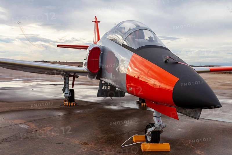 A vibrant military jet at Torrejon Air Base in Spain, an impressive part of an air show exhibition. The aircraft's bold colors stand out against the cloudy sky