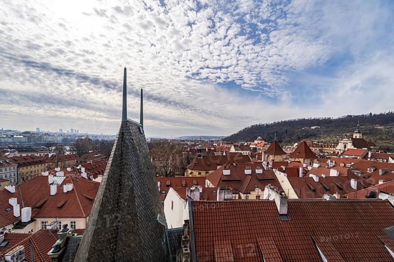 Captivating aerial shot showcasing the bustling rooftops of Prague, highlighted by a scenic backdrop of lush hills and textured clouds