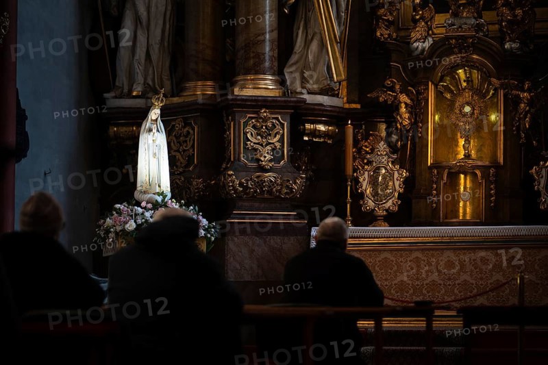 Devout people praying in a dim baroque church before the Blessed Sacrament and a statue of the Virgin Mary in Trzebnica, Poland