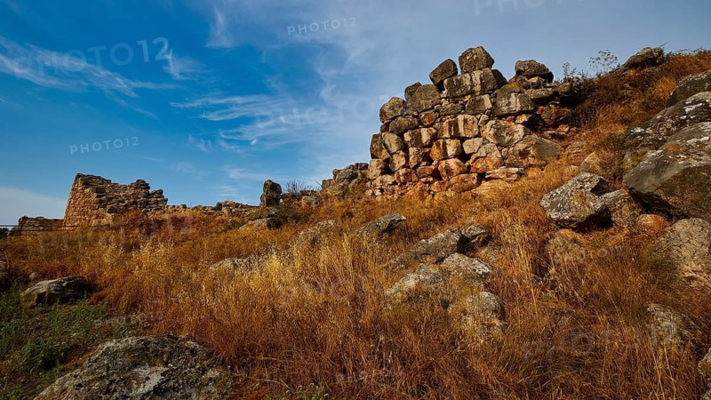 Old stone ruins on a hill with dry grass and blue sky, Tiryns, ancient city in Argolis, Mycenaean, Peloponnese, Greece