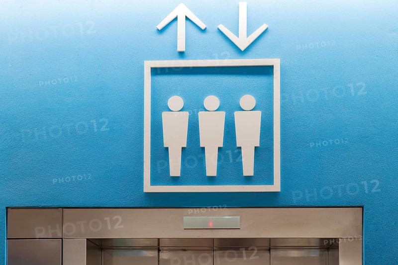 Contemporary elevator signage with up and down arrows above an entrance in a modern airport terminal, demonstrating clear directional guidance for passengers