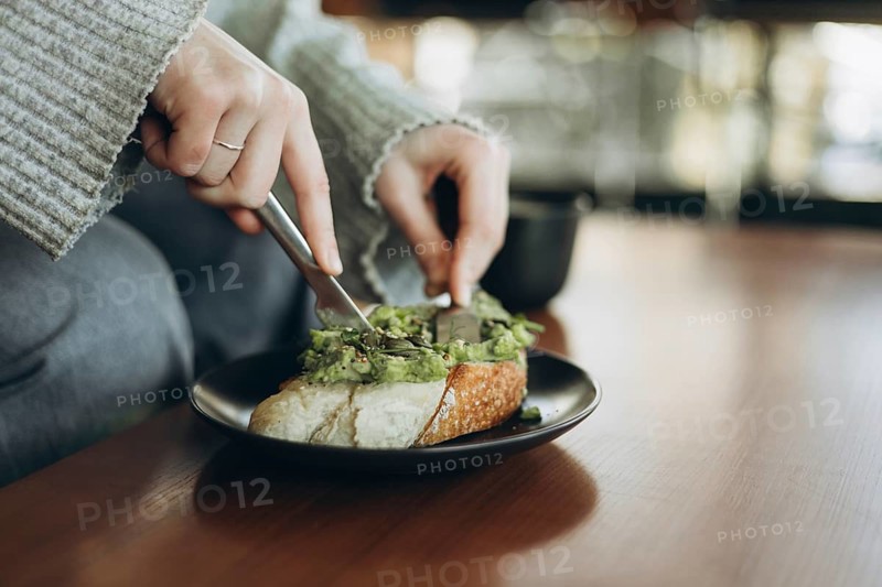 A person spreads fresh mashed avocado on a slice of crusty bread with a knife. The scene exudes a cozy and inviting atmosphere, perfect for breakfast or a light snack