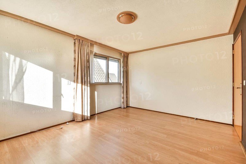 A spacious, bright, and minimalist empty room featuring natural light shining through a window, showcasing wooden flooring and simple decor