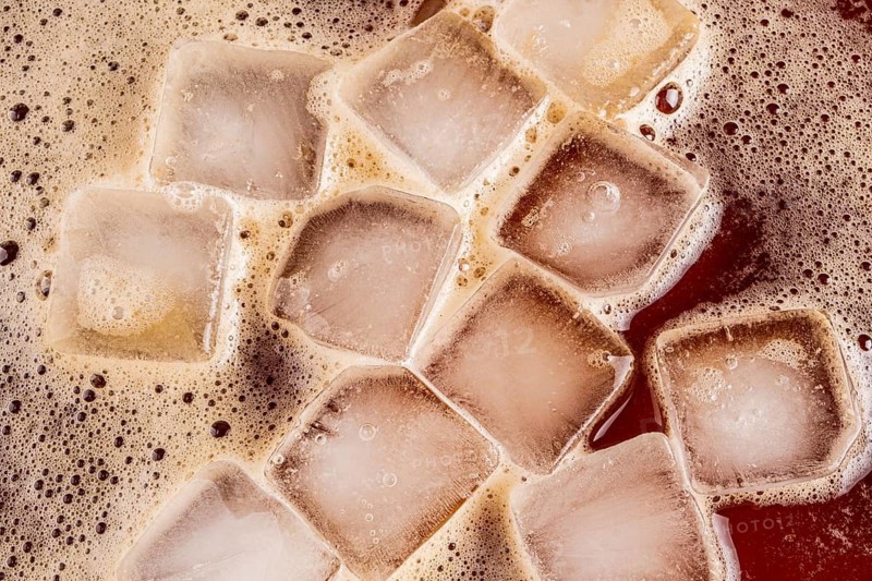 A close-up image of iced coffee with floating ice cubes. The ice cubes create a refreshing visual contrast against the dark, rich brown coffee, offering a cooling sensation