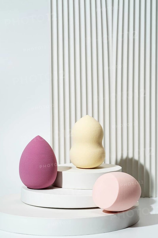 Pastel-colored cosmetic sponges arranged on white geometric platforms against a textured white background Perfect for beauty, skincare, and makeup-themed projects
