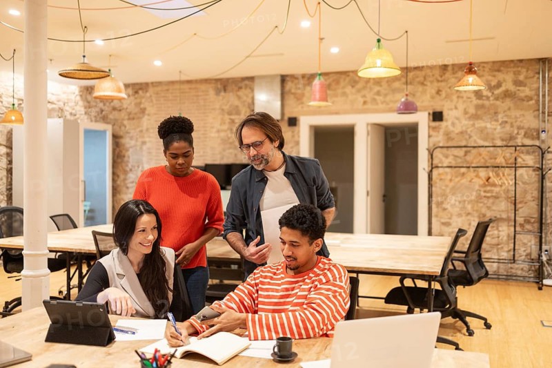 A diverse group of professionals collaborate in a stylish coworking space With a warm ambiance, they engage in discussion, contributing ideas and fostering teamwork in a modern workplace