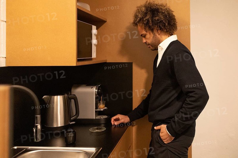 A professional in a Barcelona coworking space prepares coffee in a shared kitchen area. The modern setting includes a coffee machine and a kettle, creating a productive atmosphere