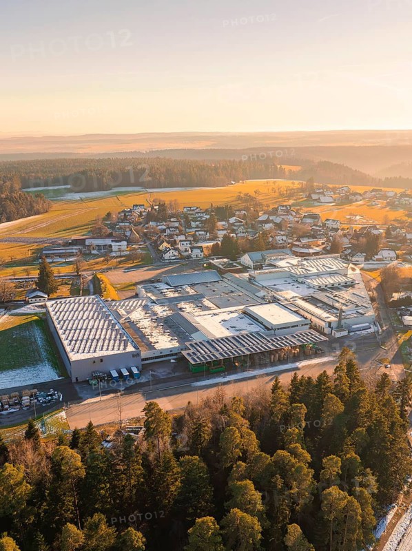 Industrial site in winter landscape, surrounded by trees and houses at sunset, Neuweiler, district of Calw, Black Forest, Germany