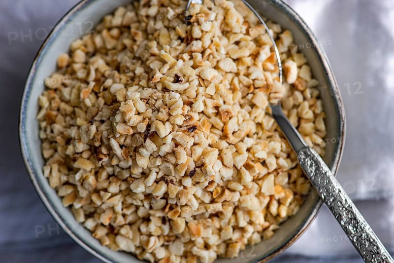 Top view of finely chopped hazelnuts in a rustic bowl with a silver spoon, ideal for baking and cooking projects