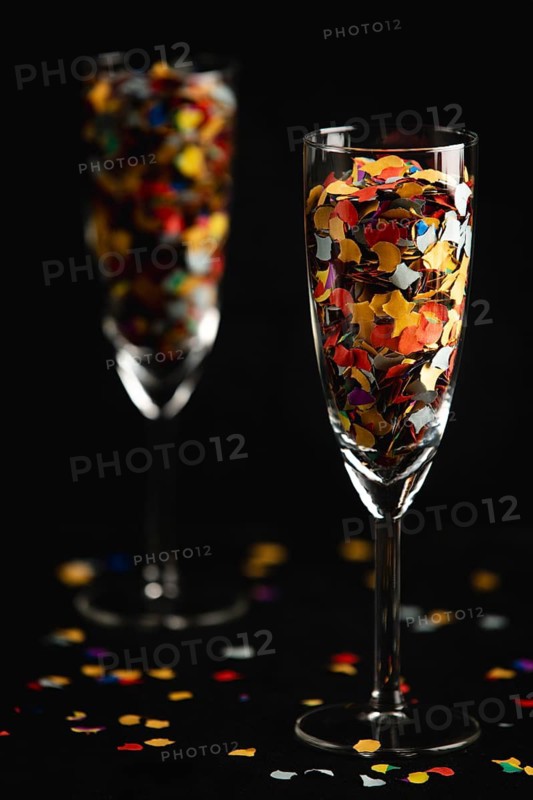 Champagne glasses filled with colourful confetti, confetti scattered on a black background