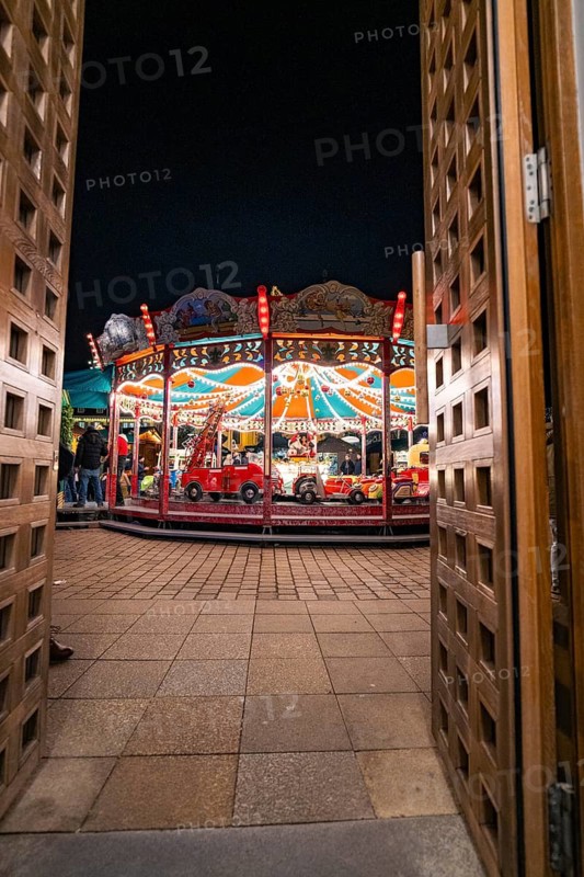 View through wooden doors onto an illuminated carousel at night, Ludwigsburg Christmas Market, Germany