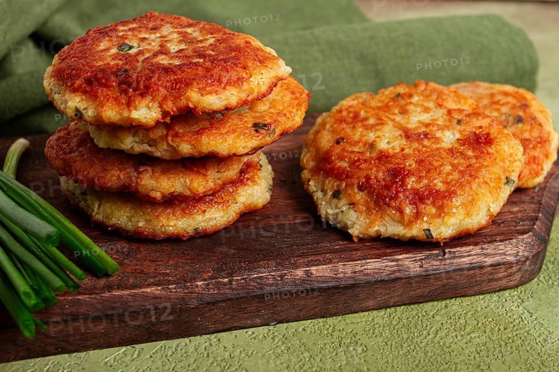 Crispy potato pancakes Latkes, stacked on a wooden board next to fresh green onions, natural light, homemade, no people