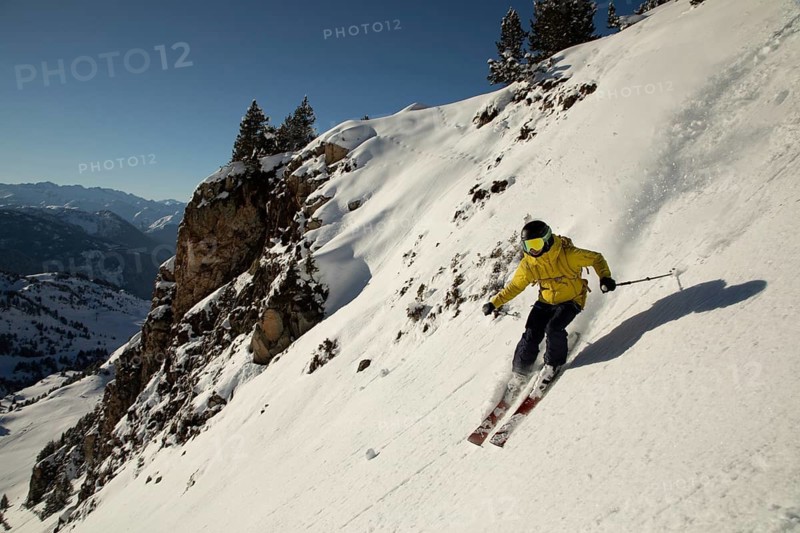 A thrilling image of a skier gliding down a steep, snowy mountain slope in bright sunlight The skier's dynamic pose and vibrant gear create an exciting freeride scene