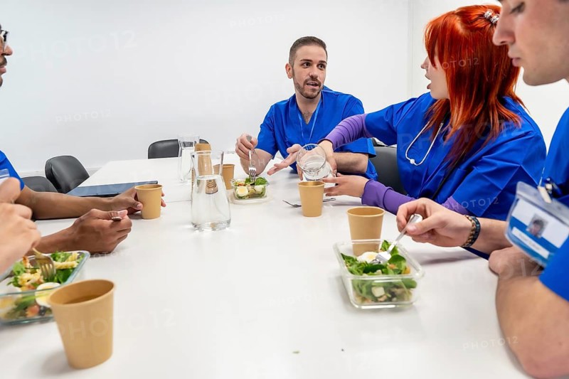 Healthcare professionals in blue scrubs enjoying a healthy salad and conversation during their well deserved lunch break at a clinic or hospital cafeteria