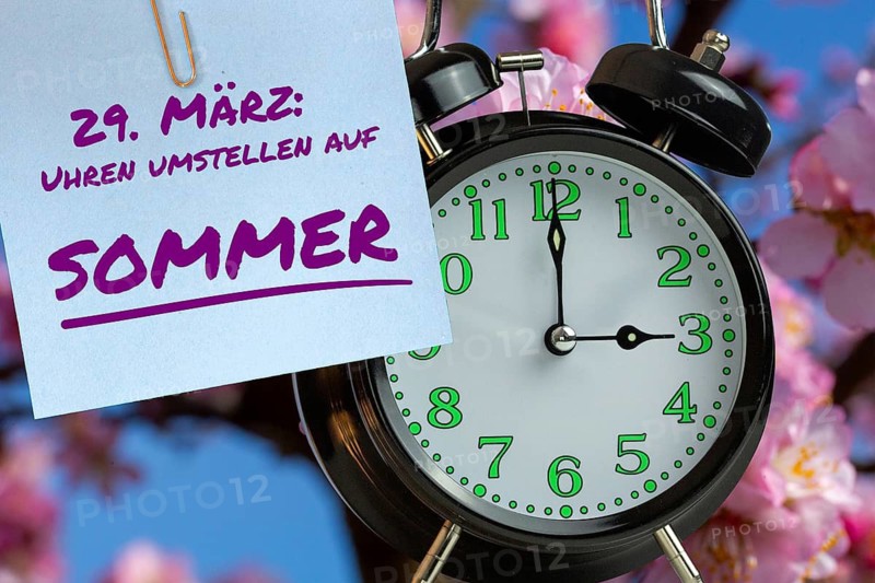 (Photo montage) Summer time change Symbolic image: Alarm in front of almond blossom and text MARCH 29 SWITCH CLOCKS TO SUMMER