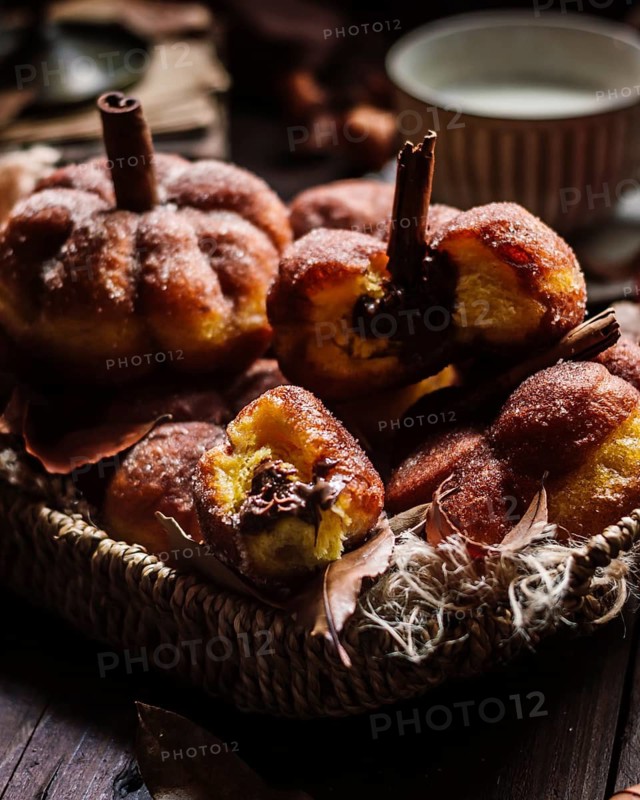 A cozy basket filled with homemade pumpkin-shaped donuts, garnished with sugar and a touch of cinnamon. The warm and inviting arrangement is perfect for autumn gatherings