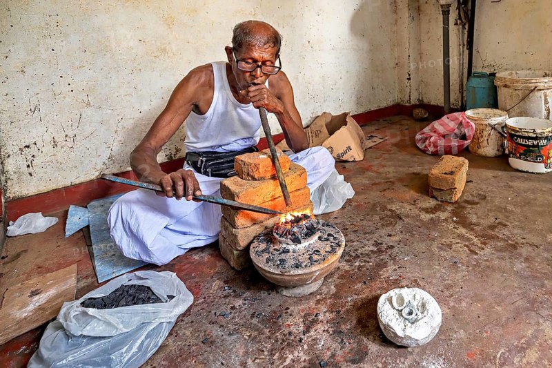 In the workshop, a man blows a pipe into a coal-fired basin, a man burns safire in a small stove in the town of Ratnapura in Sri Lanka