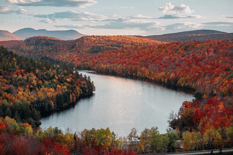 Stunning autumn foliage in Quebec showcases vibrant shades of orange, red, and yellow surrounding a serene river, creating a breathtaking natural panorama under a clear sky