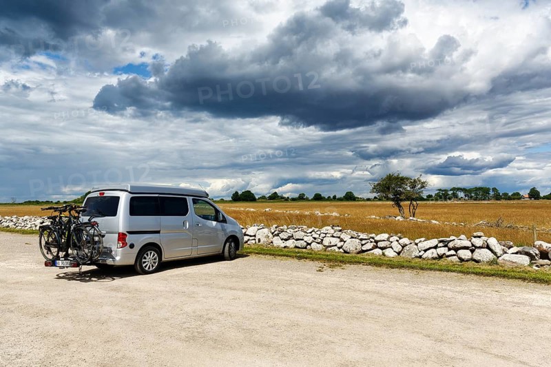 Compact campervan, camper with pop-up roof, Nissan NV200 mini camper, bicycles, bicycle rack, parking, barren limestone landscape, Stora Alvaret, UNESCO World Heritage Agricultural Landscape of South Öland, dramatic cloudy sky, Ottenby Lund, Südoeland, Öland island, Kalmar län, Sweden