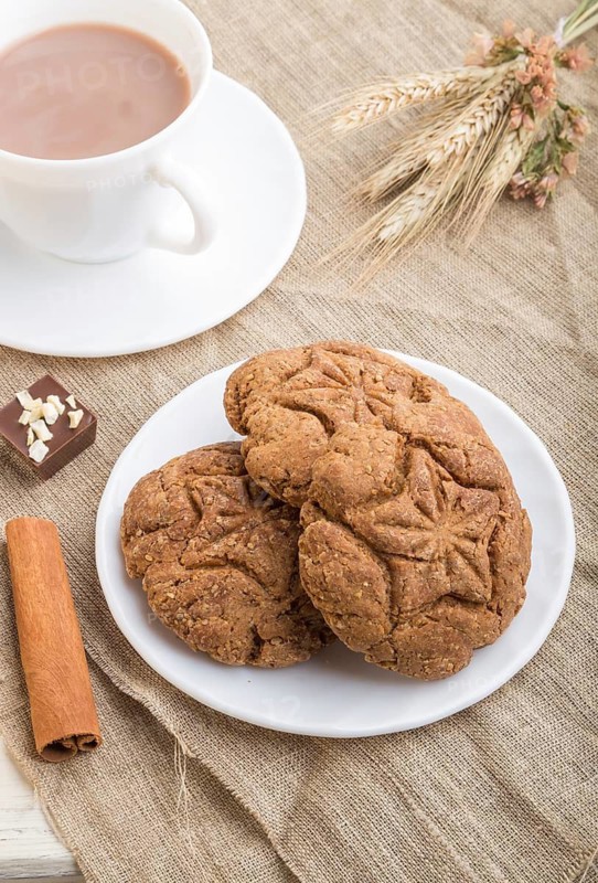 Homemade oatmeal cookies with a cup of cocoa on a linen textile and white wooden background. side view, close up