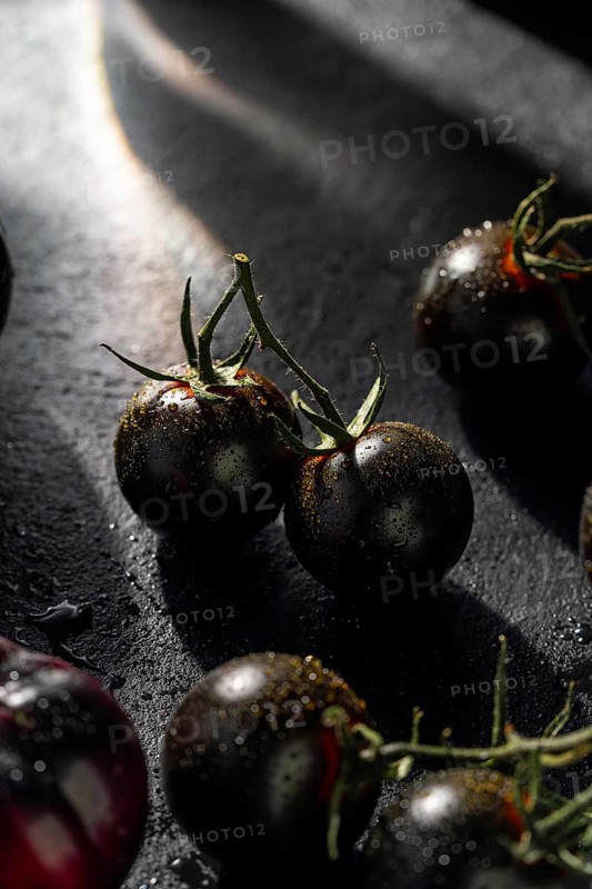 Close up of fresh black tomatoes on a dark surface, with water droplets and dramatic lighting. The image captures the vibrant, rich texture and gloss of the tomatoes