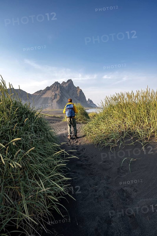 Tourist on a sand dune, Black beach with volcanic sand, Sand beach, Dunes with grass, Stokksnes headland, Klifatindur mountain range, Austurland, East Iceland, Iceland