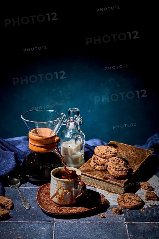 A cozy setting featuring a splash of fresh coffee in a ceramic mug, with a stack of chocolate cookies and a bottle of milk nearby, evoking warmth and comfort