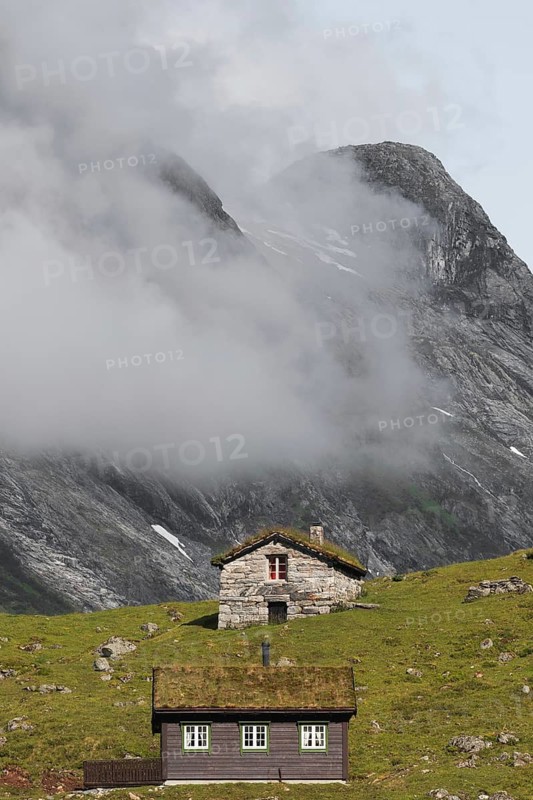 Idyllic cabins amidst green hills and foggy mountains in Norway, offering a picturesque view perfect for trekking and camping enthusiasts Ideal for outdoor adventure themes