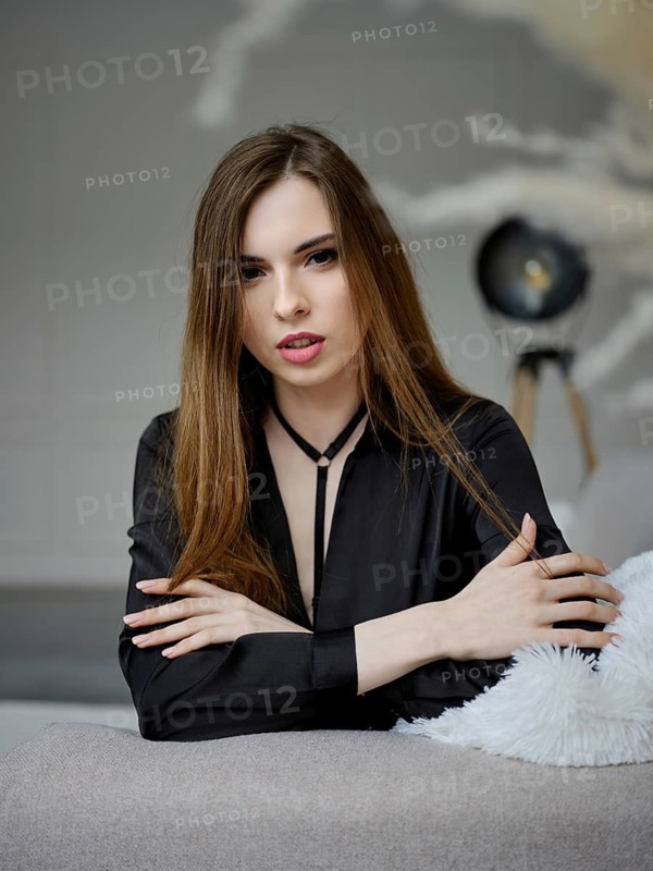 Cute young woman sitting on sofa and looking straight to the camera