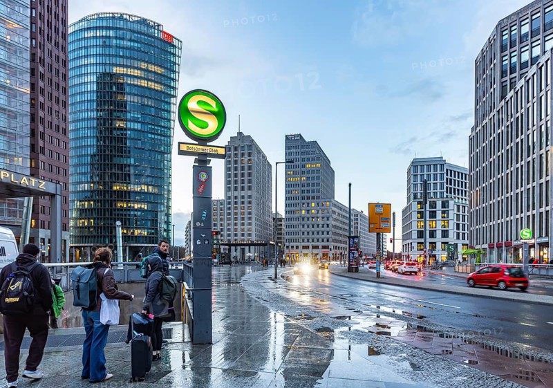 Potsdamer Platz Berlin in the evening with traffic on the streets. When it rains, the skyscrapers are reflected in puddles of water. Bahn-Tower, headquarters of Deutsche Bahn AG. Illuminated S-Bahn sign. Berlin, Germany