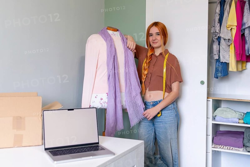 Young woman organizing her closet, preparing clothes for sale. A laptop and boxes are ready for online selling, showcasing a tidy and organized space