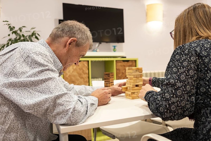 Couple with intellectual disabilities engage in a fun game of Jenga, focusing intently as they strategy their next move. The cozy indoor setting adds warmth to their interaction