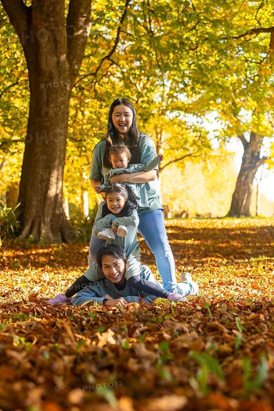Asian family of four delights in a playful autumn day outdoors, surrounded by colorful falling leaves in the park. They create joyful memories together, embracing the beauty of the season
