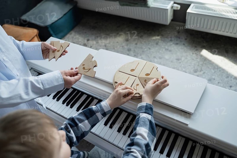 A young boy engages with music through playful learning, arranging puzzle pieces on a piano. This interactive method introduces rhythm and notes, combining fun with education