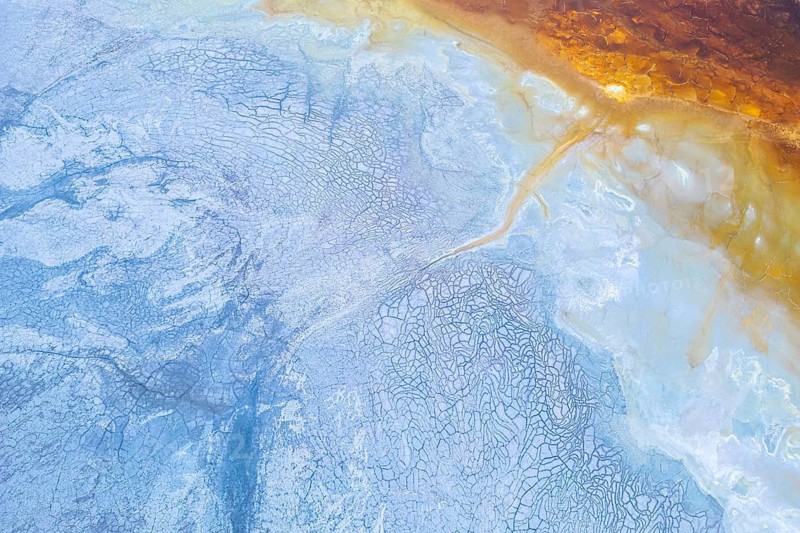 Aerial view showcasing vibrant geological formations with a striking contrast of blue and orange hues. The natural patterns create an abstract and mesmerizing landscape