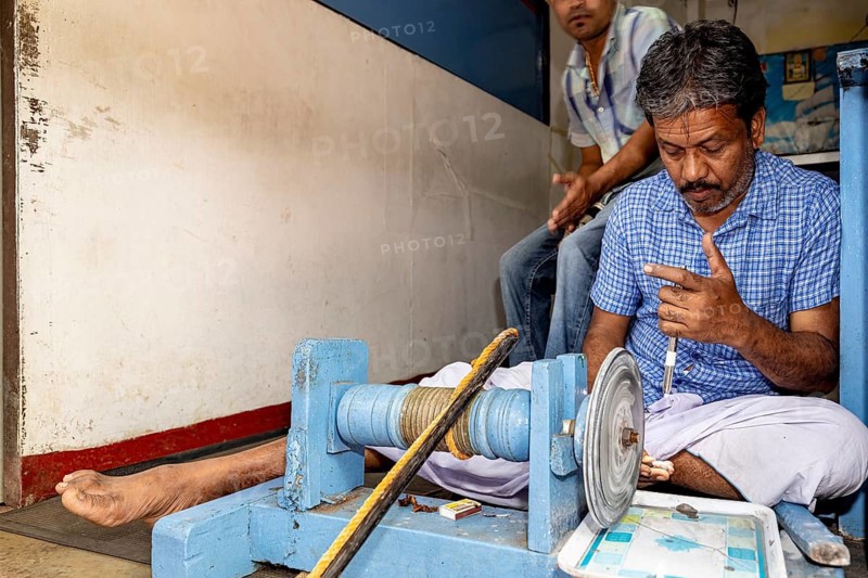 A seated man works on a machine, shows finger positions and is concentrated, the gemstone cutters in the city of Ratnapura in Sri Lanka