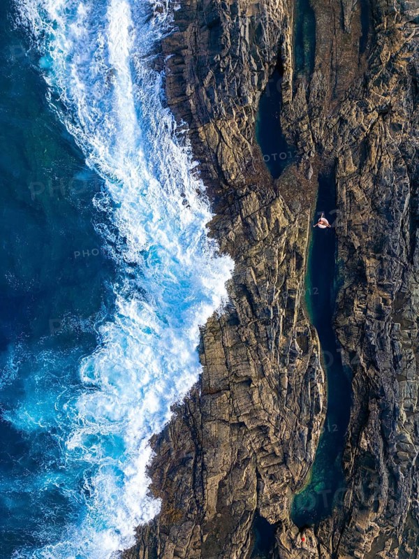 Top aerial drone view of an anonymous woman relaxing on an inflatable float in a natural pool among rugged cliffs at Tindaya Beach, Fuerteventura