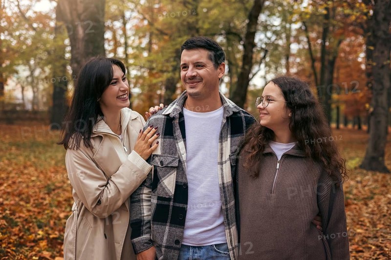 A cheerful family walks together in a park surrounded by vibrant autumn leaves. Their smiles reflect warmth and togetherness, embodying the cozy essence of fall