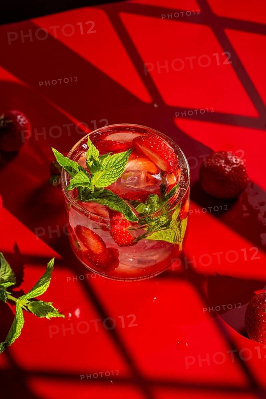 From above refreshing strawberry mojito cocktail garnished with mint, set against a vivid red background. The drink features sliced strawberries and fresh mint, evoking vibrant summer vibes