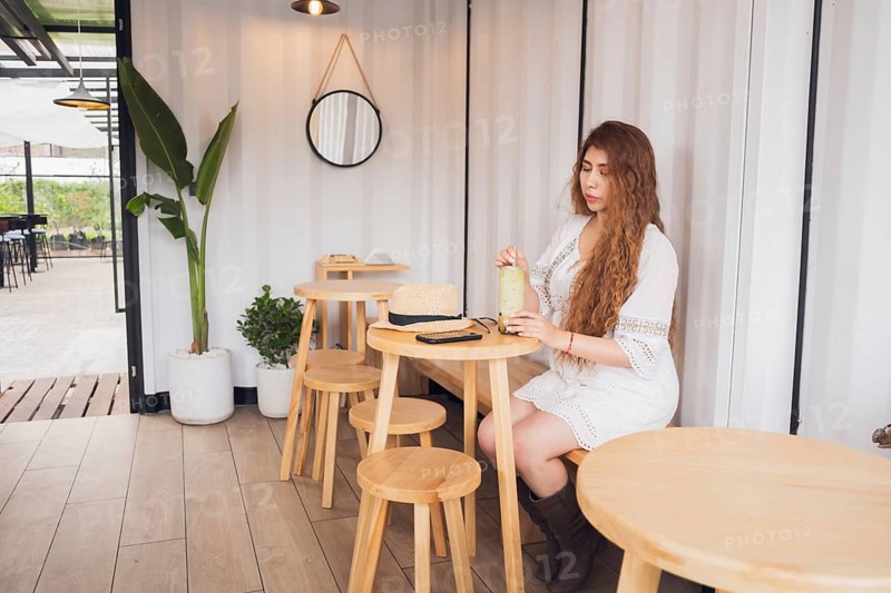 A young American Latin woman with long hair enjoys a refreshing drink at a cozy cafe. Surrounded by modern decor, she embodies relaxation and a trendy lifestyle