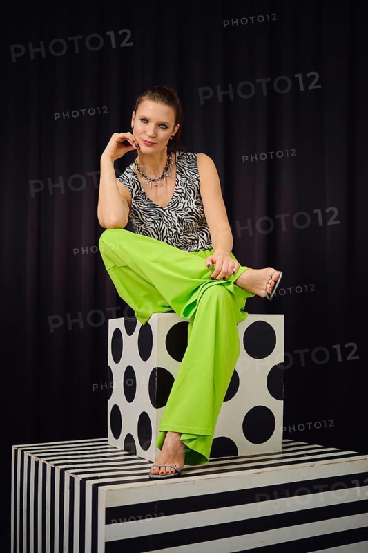 A woman sits on a patterned cube in a trendy outfit composed of a zebra print top and neon green wide-leg pants