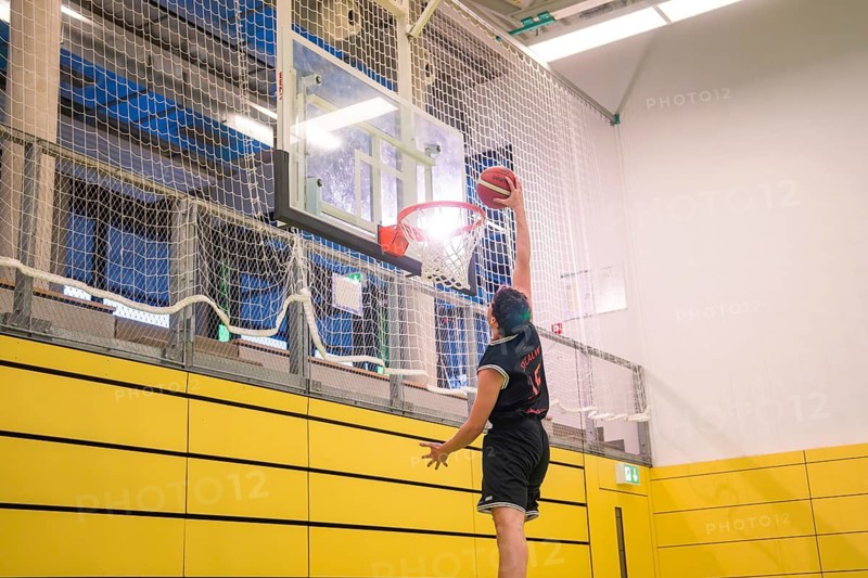 A player energetically places the ball in the basket in a yellow gym, basketball TSV Calw, Germany