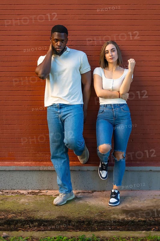 Vertical full length photo of a multi-ethnic models with denim clothes standing leaning on urban wall