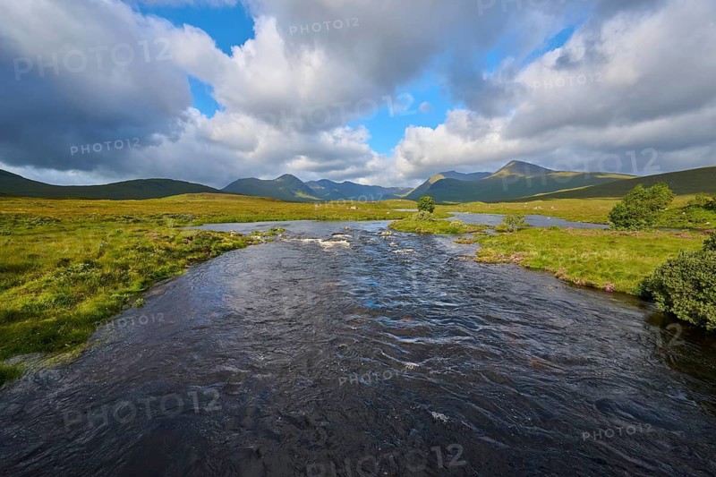 River flows through green landscape under sky with clouds, Rannoch Moor, Bridge of Orchy, Scotland, United Kingdom, United Kingdom