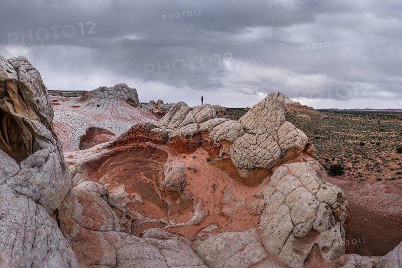 Unrecognizable person standing on a peak of strikingly textured rock formations at White Pocket, Arizona, USA. The overcast sky complements the surreal, colorful landscape