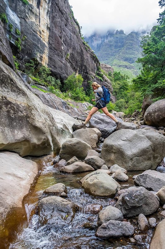 Female hiker jumping over rocks, Tugela Gorge or Tugela Gorge in the riverbed, Drakensberg National Park, KwaZulu Natal, South Africa