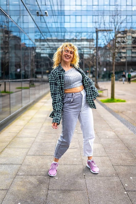 Caucasian woman with blond curly hair dancing in urban style in a city street wearing casual clothes